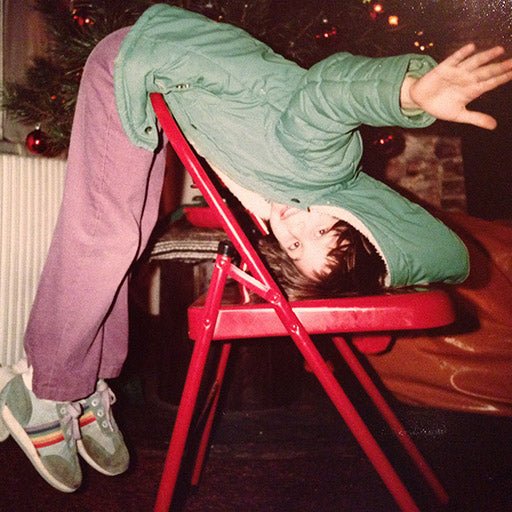 Photo of business owner as a kid playing over a red chair with 80's rainbow shoes, and a festive 80's background